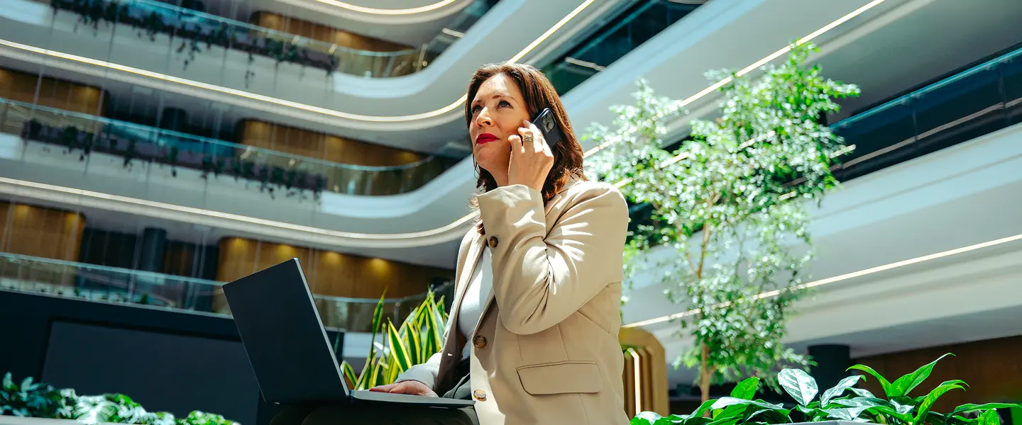 una donna d'affari sta lavorando in un non-luogo e ha il computer portatile appoggiato sulle gambe mentre risponde al telefono